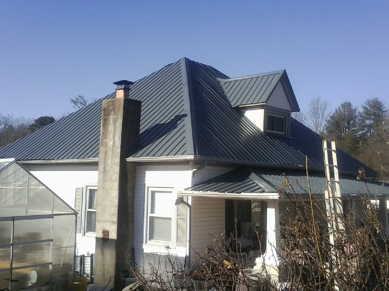 Dark blue standing seam metal roof on a white farmhouse with dormer — Slate & Tile Roof Repair by Roofing Brothers in Tougaloo