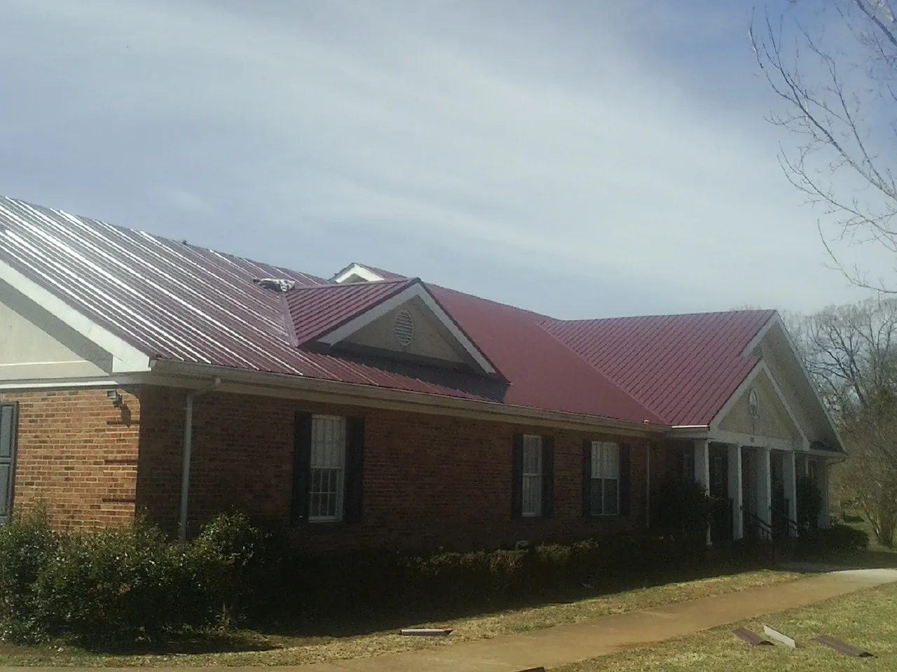Red metal roof with gabled entries on a long brick building, from a Hail Damage Roof Repair job in Tougaloo