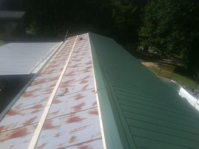 Old rusted panels beside newly installed green metal roofing — Wind Damage Roof Repair by Roofing Brothers in Tougaloo