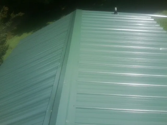 New green metal panels meeting at the ridge of a roof — Flat Roof Repair work by our crew in Tougaloo