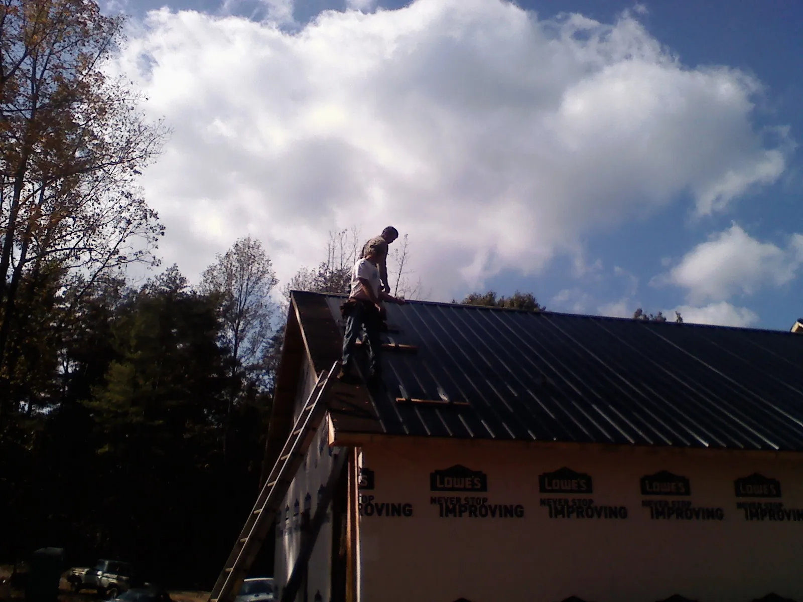 Roofer fastening dark metal panels high against a cloudy sky, from a Roof Inspection job in Tougaloo