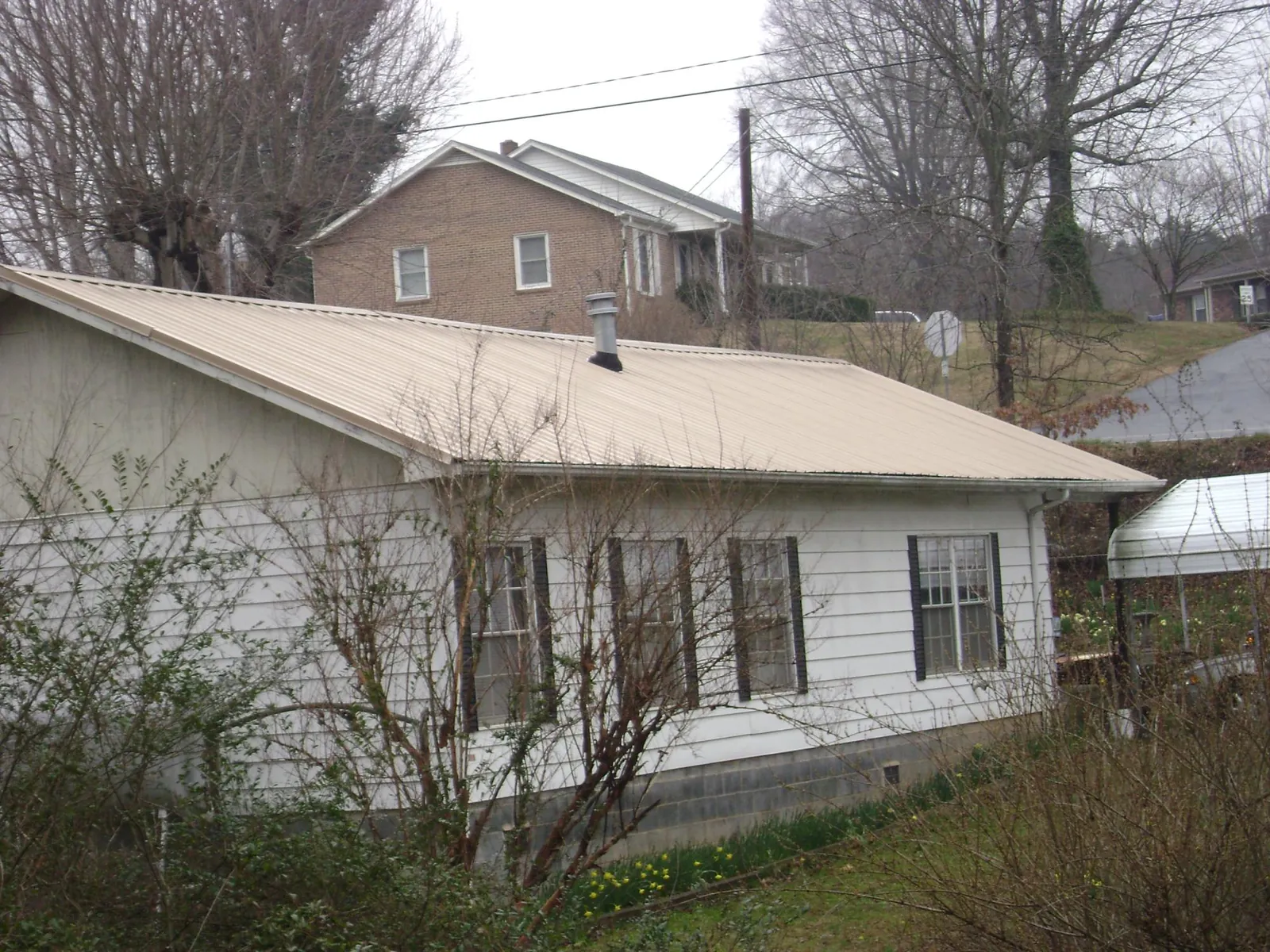 Tan metal roof on a white sided house set into a hillside — Commercial Roofing by Roofing Brothers in Tougaloo